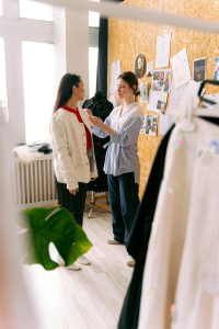 A fashion designer adjusts a model's outfit in a creative studio space filled with inspiration boards.