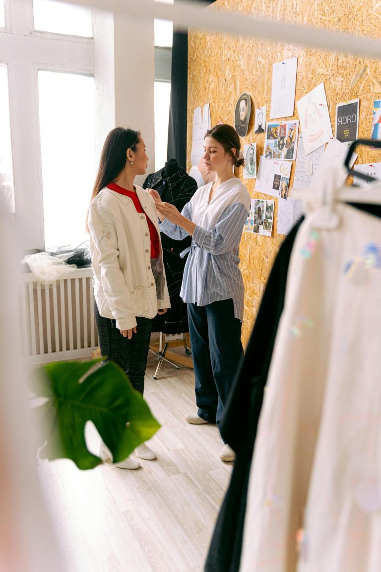 A fashion designer adjusts a model's outfit in a creative studio space filled with inspiration boards.