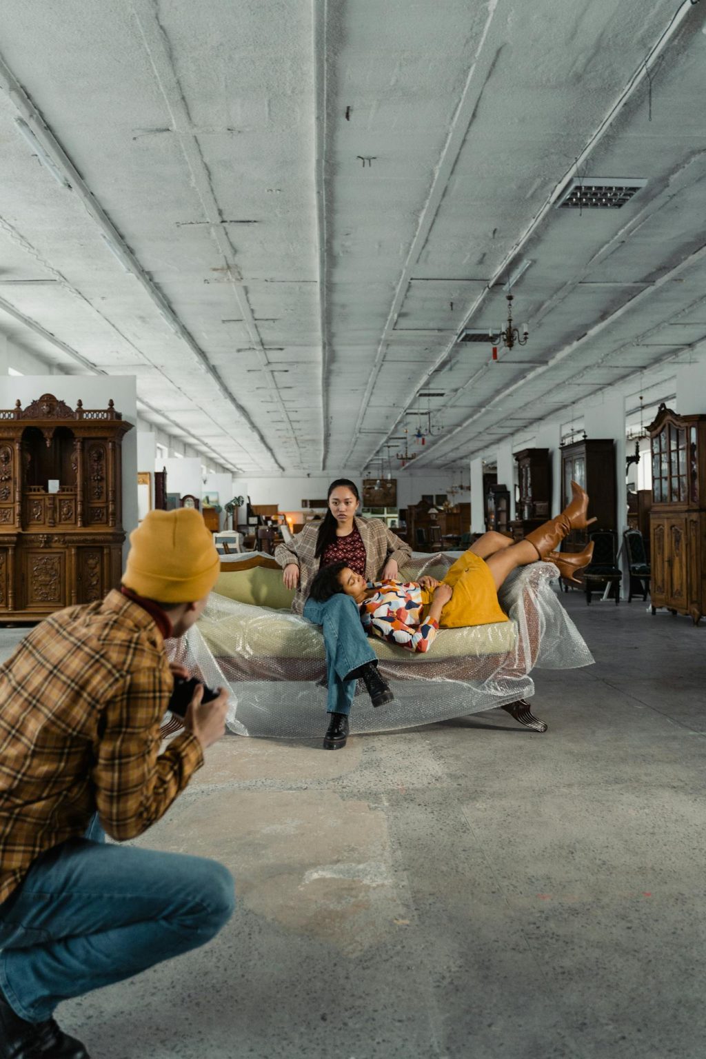 Model posing on vintage furniture with photographer capturing the scene in atmospheric warehouse.